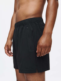 Model side view wearing Zephyr 5" Short in Black, featuring zippered pockets and drawstring waist.